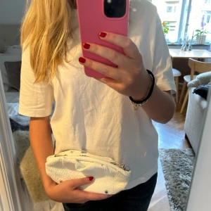 Vit axelväska med kedja från Nunoo - Vit axelväska från Nunoo i skinn med silverfärgad kedja. Väskan har en perfekt storlek för mobilen och det viktigaste, supernajs att använda som en clutch! Väskan har inga defekter och är i nyskick! 