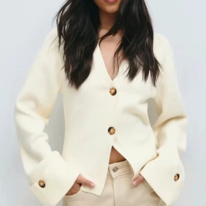 Beige kofta - Säljer en beige kofta med v-ringning och stora bruna knappar framtill och på ärmsluten. Koftan har lång ärm och en loose passform som ger en chill vibe. Perfekt att slänga på sig när det är lite kyligt ute.