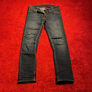 Mörkblå jeans från Nudie Jeans, 27/30 - Snygga mörkblå jeans från Nudie Jeans i klassisk modell med orangea sömmar och raka ben. Jeansen har fem fickor och är tillverkade i slitstarkt denim. Perfekta för dig som gillar en tidlös och clean look.