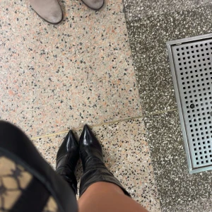 Svarta stövlar med spetsig tå och klack - Snygga svarta stövlar i skinn med spetsig tå och hög klack. Klassisk modell som går upp till knäet och ger en edgy vibe till varje outfit. Perfekta till kjol eller klänning för en trendig look.