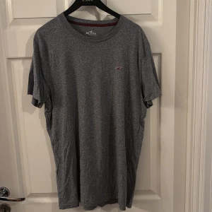 Grå t-shirt från Hollister - En stilren grå t-shirt från Hollister med liten broderad logga på bröstet. Klassisk rund halsringning och korta ärmar. Skön passform och tillverkad i mjuk bomull, perfekt för en chill och avslappnad look.