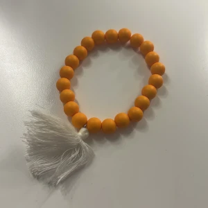Orange pärlarmband med vit tofs - Coolt armband med runda orange pärlor och en vit tofs som detalj. Perfekt för dig som gillar färgglada accessoarer och vill sticka ut lite extra. Tofsen ger en lekfull vibe till din stil. OBS, katt finns i hemmet.