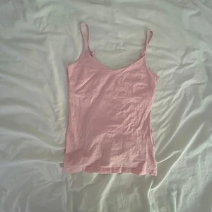 Ljusrosa linnetopp med smala axelband - Säljer en söt ljusrosa linnetopp med smala, justerbara axelband och v-ringad hals. Toppen är enkel och stilren, perfekt att matcha med jeans eller kjol. Tillverkad i mjuk bomull som känns skön mot huden.