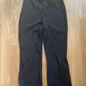 Svarta ribbade byxor med vida ben - Säljer ett par svarta byxor med breda ribbade ränder och skön, lite lös passform. Byxorna har vida ben och är perfekta för en chill och trendig look. Passar dig som gillar stilrena och bekväma plagg.