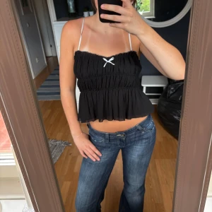 Jättesöt Zara topp med volang och rosett - Supersöt svart topp från Zara med tunna axelband och volang design. Använd några fåtal gånger!!