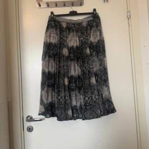 Plisserad långkjol med ormmönster - Halvt Plisserad långkjol med svart, grått och beige ormmönster. Kjolen har ett glittrigt resårband i midjan och är tillverkad i ett lätt, flowy material. Perfekt för dig som vill sticka ut med en edgy vibe. Från märket cream i storlek 38/M. Mycket fint skick, jag hittar inga synliga anmärkningar eller defekter. 