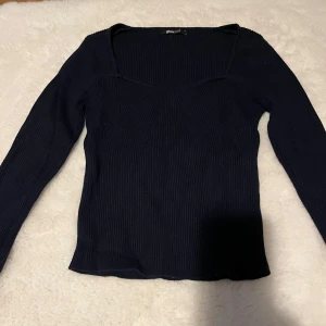Mörkblå ribbad topp från Gina Tricot - Säljer en mörkblå långärmad topp från Gina Tricot med fyrkantig ringning. Toppen är ribbad och har en slim passform som sitter snyggt på kroppen. Perfekt att styla med jeans eller kjol för en clean look.