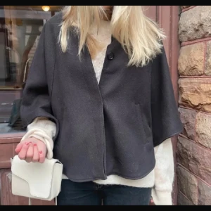 Poncho kappa  - Snygg svart poncho kappa med korta, vida ärmar och tre knappar framtill.  Enkel och stilren design. 