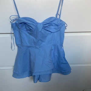 Zara topp - Supersöt ljusblå korsett-topp med tunna axelband och volang nertill. Toppen har snygga sömdetaljer och en draperad byst som ger en feminin look. Perfekt för dig som vill sticka ut med en trendig och somrig vibe.