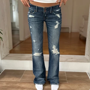 Abercrombie & fitch Lågmidjade jeans med slitningar - Ett par lågmidjade jeans med slitningar från Abercrombie & fitch i storlek ”0” ~ XXS/XS. Jeansen är i fint skick förutom skador längst ner på benen (se bild). Rakt över midjemått: 37cm. Gren: 17cm. Innebenslängd: 80cm. Tips: jag på bilden är 165, dessa släpar då lite på golvet för mig. Jag skickar ditt köp inom 24h. G15