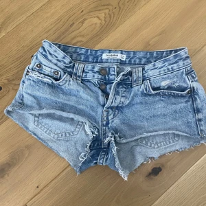 Blå jeansshorts från Pull&Bear - Snygga ljusblå jeansshorts från Pull&Bear med låg midja, råa kanter och slitna detaljer. Klassisk femficksmodell med dubbla knappar framtill och bakfickor med lock. Perfekta för varma sommardagar och en avslappnad stil.