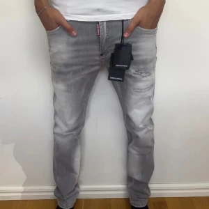 Grå Dsquared2 jeans straight fit - Snygga grå jeans från Dsquared2 med straight fit och slitna detaljer. Jeansen har klassisk femficksdesign, silverfärgad knapp och Dsquared2-logga på både fram- och baksida. Tillverkade i bomull med en cool tvättad look.