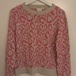 Beige och rosa leopardtröja från Vila - Snygg beige stickad tröja från Vila i storlek XS med rosa leopardmönster. Tröjan har rund halsringning, ribbade muddar och långa ärmar. Perfekt för dig som vill sticka ut med ett coolt mönster och mjuk känsla.