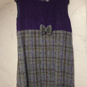 Lila och grårutig klänning från Glen Appin - Superfin kort klänning från Glen Appomin i tweedmaterial (ylle) med lila manchester upptill och klassiskt rutigt ylletyg  nertill. Söt rosettdetalj framtill. Nyskick, aldrig använd. 