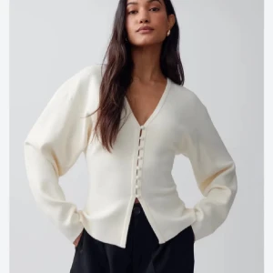 Krämvit kofta med v-ringning - Snygg krämvit kofta med v-ringad hals och knappar framtill. Modellen har långa ärmar och en något lös passform. Perfekt att styla med både jeans och kjol för en clean look.