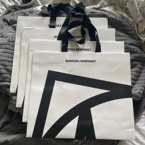 Shoppingväska Nordiska Kompaniet - Säljer flera stora shoppingväskor från Nordiska Kompaniet i vitt med svart grafiskt tryck och breda svarta handtag. Perfekt för att bära hem dina nya fynd eller använda som snygg förvaringspåse. Stilren och klassisk design.