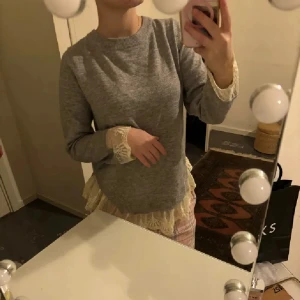 Grå stickad tröja med spets och rosett - Superfin grå stickad tröja med lång ärm och snygga spetsdetaljer vid ärmslut och nederkant. Baksidan har en öppen rygg med v-ringning och en söt rosett i nacken. Perfekt för dig som gillar romantiska och unika detaljer. Vintage❤️