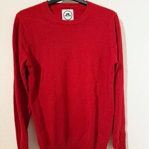 Röd kashmirtröja J.Lindeberg - Riktigt mjuk och lyxig röd tröja från J.Lindeberg i 100% kashmir. Klassisk rund halsringning, ribbade muddar och långärmad modell. 