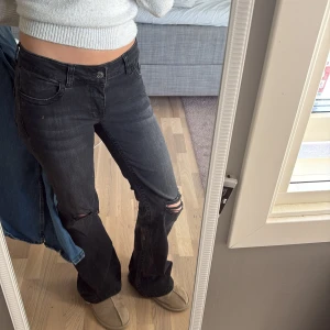 Svarta bootcut jeans med slitning - Säljer ett par svarta bootcut jeans med snygg slitning på knäet. Jeansen har låg midja och klassisk femficksdesign. Materialet är jeans i bomull och de har en lite tvättad look som ger en cool vibe. Säljer pga för stor storlek❤️(PS: pris kan diskuteras 🥰)