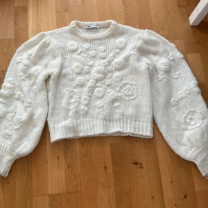 Vit stickad tröja med blommor från Zara - Superfin vit stickad tröja från Zara med puffiga långärmar och broderade blommor över hela tröjan. Croppad modell med ribbad kant vid hals och nederdel. Perfekt för dig som gillar romantiska detaljer och vill ha en mysig look. skicket syns på bilderna