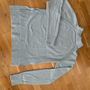 Ljusgrå stickad tröja från Dagmar - Säljer en ljusgrå/ljusblå stickad polotröja från Dagmar i storlek S. Tröjan har ribbade muddar och bred ribbad kant nedtill, samt långärmad design.