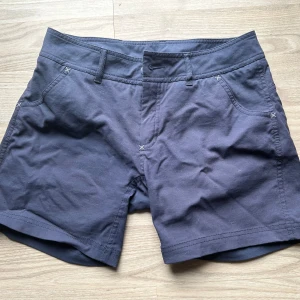 Mörkblå shorts från Houdini, dam stl S - Snygga mörkblå shorts från Houdini i klassisk modell med fyra fickor och bälteshällor. Tillverkade i mjuk bomullsmix som känns skön mot huden. Perfekta för sommardagar och äventyr utomhus. Stilren design med diskreta sömdetaljer och normal passform.