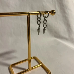 Silvriga örhängen med kedjor och spikes - Snygga silvriga örhängen med små kedjor och spetsiga spikes som hänger ner. Perfekt för dig som gillar en edgy och cool stil. Örhängena är i metall och har en minimalistisk design med runda ringar och konformade detaljer.
