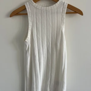 Vit ribbad linnetopp från H&M - Säljer en vit ribbad linnetopp från H&M. Toppen är ärmlös med rund halsringning och har en snygg, stickad struktur som ger en clean och fräsch look. Perfekt att styla med jeans eller kjol för en enkel men trendig outfit.