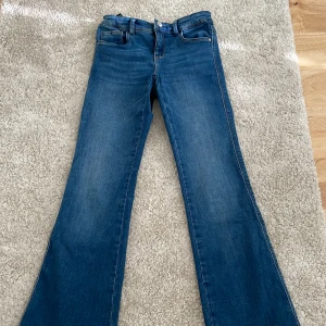 Blå bootcut jeans 146 - Snygga blå jeans i bootcut-modell med klassisk femficksdesign och normal passform. Jeansen har en något utsvängd benslut och är tillverkade i slitstarkt denimtyg. Perfekta för dig som gillar en retro vibe och vill ha ett par bekväma jeans till vardags.