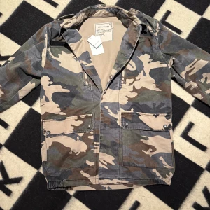 Camouflage overshirt från Zadig & Voltaire - Snygg overshirt från Zadig & Voltaire i klassiskt camouflage-mönster med gröna, bruna och beige toner. Jackan har stora fickor framtill med tryckknappar och dragkedja. Perfekt för dig som vill ha en cool och avslappnad look. Storlek XS men sitter som en M!