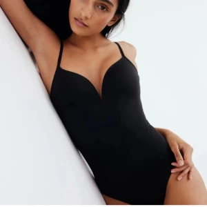 Svart bodysuit med smala axelband - Snygg svart bodysuit med smala axelband och v-ringad design. Perfekt för att bära under kläder eller som en del av en outfit. Den har en tight passform som framhäver figuren. Den är i storlek m men passar mig som har S