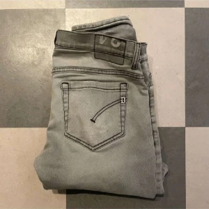 Dondup jeans - Snygga grå jeansbyxor med en slim passform. Byxorna har en klassisk femficksdesign och en diskret slitning på ena benet. Perfekta för en stilren look.