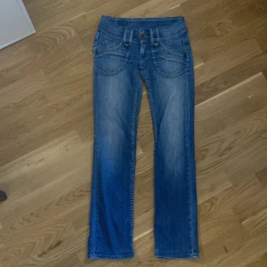 Blå jeans  - Snygga blå jeans. De har en klassisk femficksdesign och knappar fram. Perfekta för en avslappnad stil.