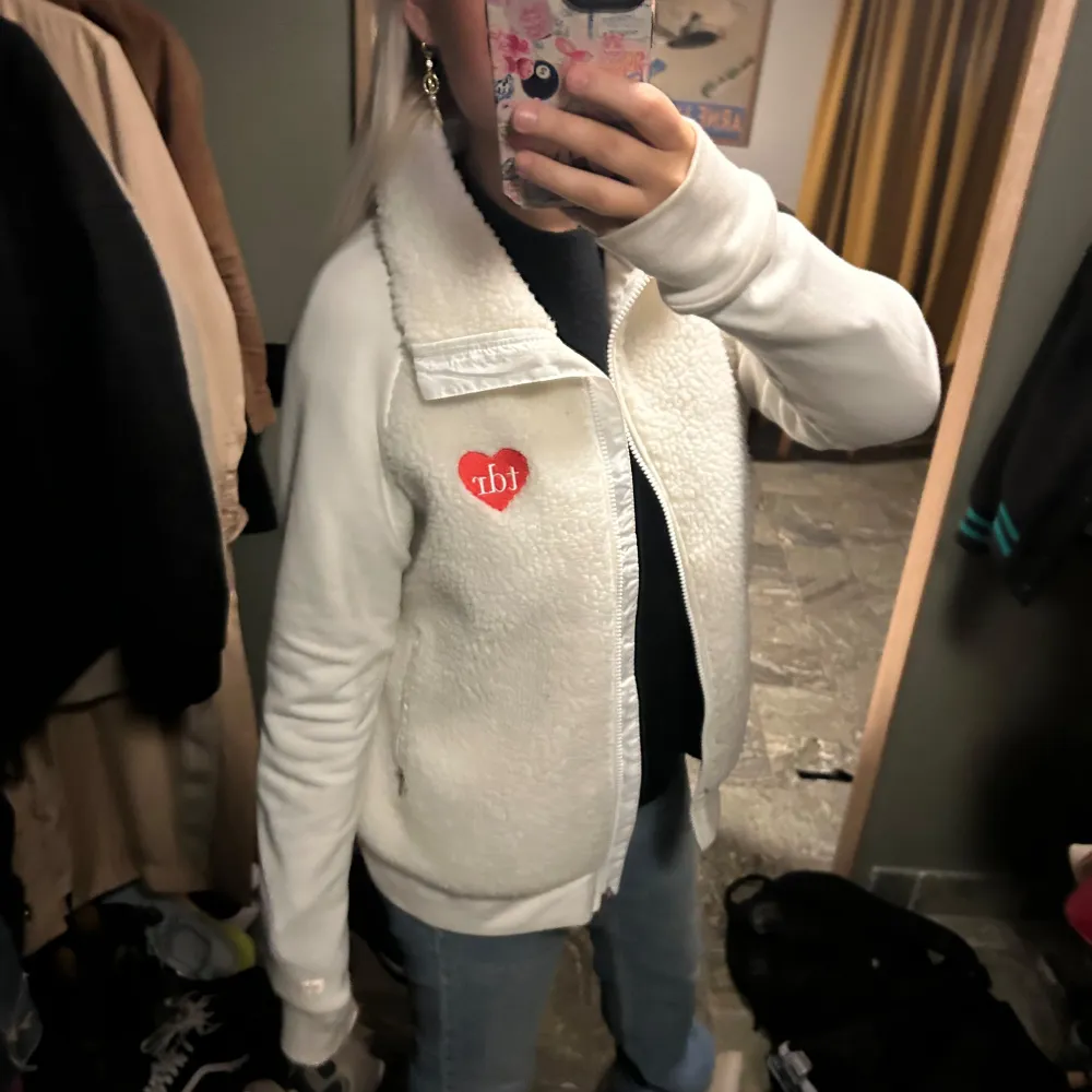 Säljer en mysig vit fleecejacka med dragkedja och en söt hjärtdetalj på bröstet. Jackan har långa ärmar och en hög krage som håller dig varm. Köpt i new York för 60$. Känner inte igen märket. . Takit.