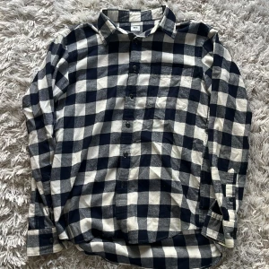 Blåvit rutig skjorta från Uniqlo - Säljer en klassisk blåvit rutig skjorta från Uniqlo. Skjortan har långa ärmar och knappar framtill. Perfekt för en avslappnad stil.