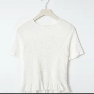 Smockad topp - Söt vit topp med korta ärmar och volangdetalj vid nederkanten. Toppen har en texturerad yta som ger en extra touch. Perfekt för en stilren och enkel look. Den är storlek 164 och jag har storlek xs och s och den passar mig bra. Det går att få mer bilder💕💕