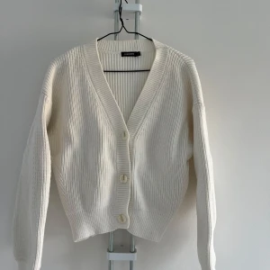 Vit ribbad kofta från J.Lindeberg - Säljer en stilren vit kofta från J.Lindeberg. Den är ribbad med en v-ringad design och knappar framtill. 