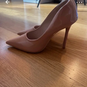 Beiga pumps med spetsig tå - Snygga beiga pumps med spetsig tå och hög klack. Perfekta för en elegant look. Tillverkade i ett glansigt material som ger en lyxig känsla.