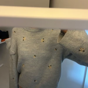 Ljusblå stickad tröja från Zara - Säljer en söt ljusblå stickad tröja från Zara med små blommiga broderier. Tröjan har långa ärmar och en rund halsringning. Den ser mer nopprig ut på bilden än i verkligheten❣️