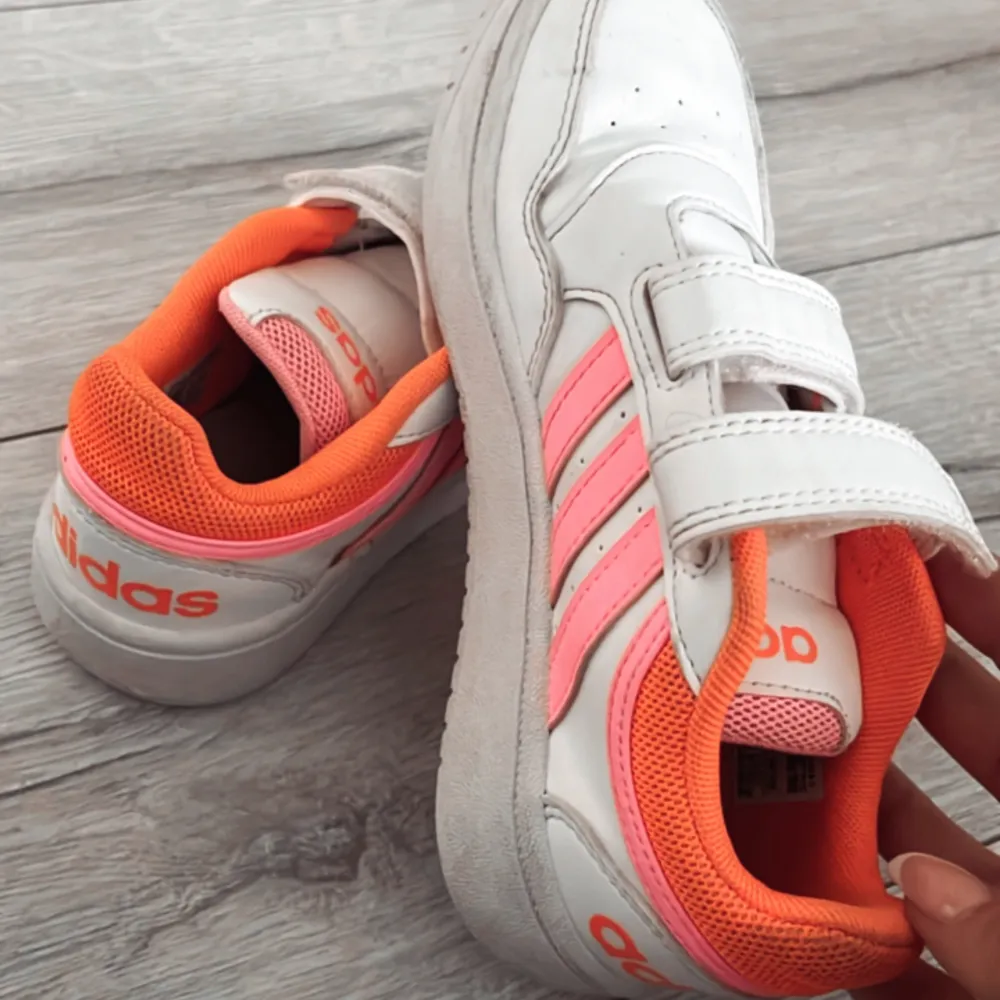 Snygga vita sneakers barn storlek från Adidas med rosa och orange detaljer. Skorna har kardborreband för enkel på- och avtagning och en bekväm passform. Knappt använda i st 31. Kengät.