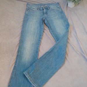 Blå bootcut jeans - Snygga blå lågmidjade bootcut jeans med klassisk femficksdesign och knappgylf. Perfekta för en avslappnad stil. De har en ljus tvätt och subtila slitningar för en trendig look. Pris kan diskuteras🥰
