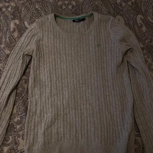 Grå ribbad tröja från Gina Tricot - Säljer en stilren grå ribbad tröja från Gina Tricot. Tröjan har långa ärmar och en rund halsringning med en grön detalj på insidan. Perfekt för en avslappnad look.