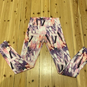 Färgglada leggings från SOC - Säljer ett par färgglada leggings från SOC med abstrakt mönster i rosa, lila och svart. Är perfekta för träning eller en färgglad vardagslook. Materialet är stretchigt och bekvämt.