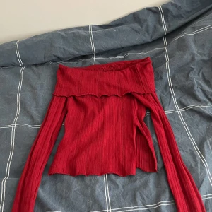 Röd ribbad offshoulder topp - Snygg röd ribbad offshoulder topp med långa ärmar. Perfekt för en stilren look. Den har en vågig kant upptill som ger en extra touch av elegans.