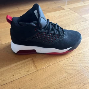 Svarta Nike Air Jordans med röda detaljer - Säljer ett par svarta Nike Air Jordans med röda detaljer. Skorna har en rund tå och snörning framtill. Sulan är vit med röda inslag och har Jumpman-loggan undertill. Perfekta för dig som vill ha en stilren och sportig look.