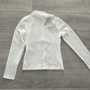 Vit långärmad topp med unik design - Säljer en vit långärmad topp med en unik design och textur. Toppen har en intressant detalj vid halsen som ger den en modern touch. Perfekt för dig som vill ha något annorlunda i garderoben!