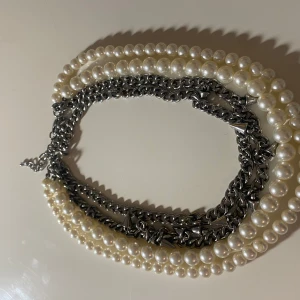 Halsband med pärlor och kedjor - Unikt halsband med en kombination av vita pärlor och silverfärgade kedjor. Detaljer med små guldfärgade nitar ger en edgy touch. Perfekt för att lyfta vilken outfit som helst.