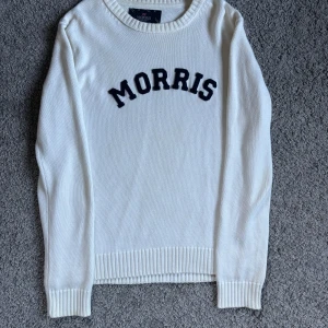 Vit tröja från Morris - Säljer en stilren vit tröja från Morris med svart text på bröstet. Tröjan har långa ärmar och ribbade muddar vid ärmslut och nederkant. Perfekt för en avslappnad och snygg look.