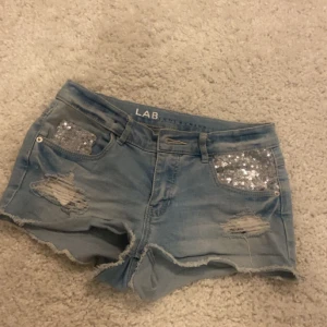 Blå jeansshorts med paljettdetaljer - Snygga blå jeansshorts från LAB med slitna detaljer och glittriga paljetter på framfickorna.  