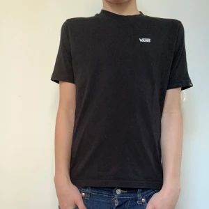 Svart t-shirt från Vans - Säljer en klassisk svart t-shirt från Vans med deras ikoniska logga tryckt på bröstet. T-shirten är kortärmad och gjord i mjuk bomull för en bekväm passform. Modellen på bilden är 163cm
